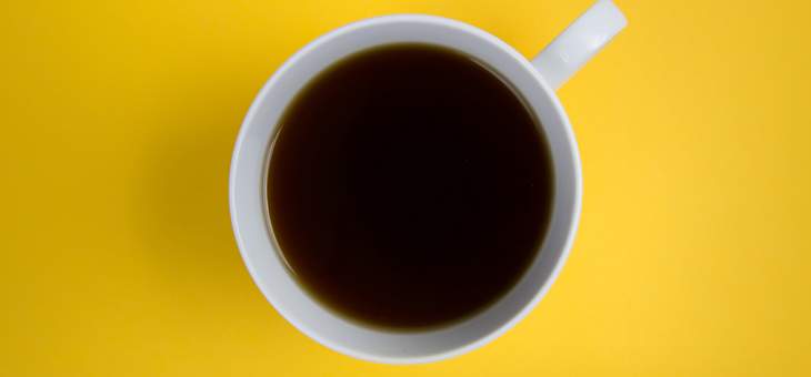 Coffee cup overhead on bright yellow background yellow-flatlay-black-coffee-cup-white-handle-mug-minimal